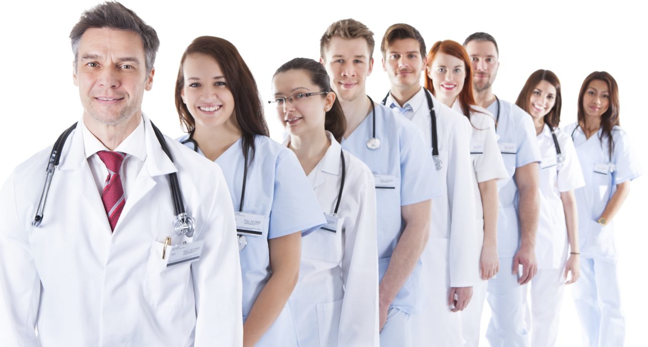 Long receding line or queue of smiling doctors and nurses in white uniforms wearing stethoscopes around their necks isolated on white
